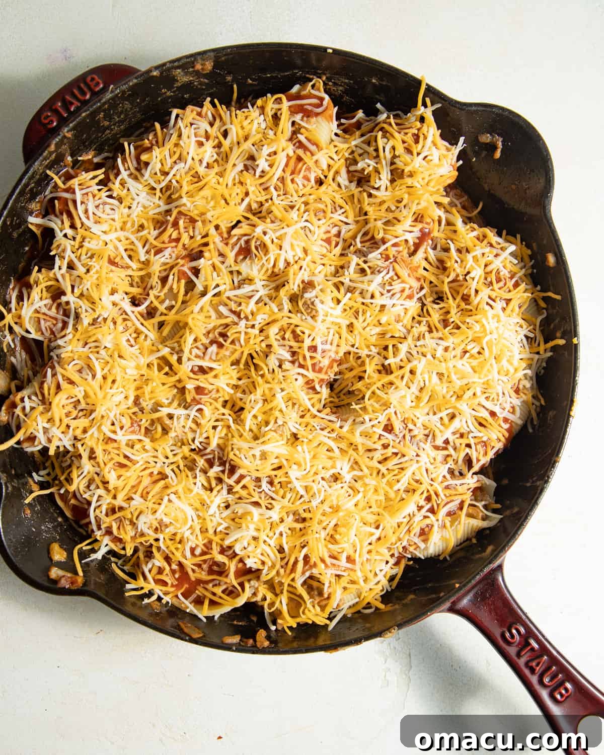 Shredded cheese covering a skillet full of Mexican stuffed shells, perfectly arranged and ready to go into the oven.