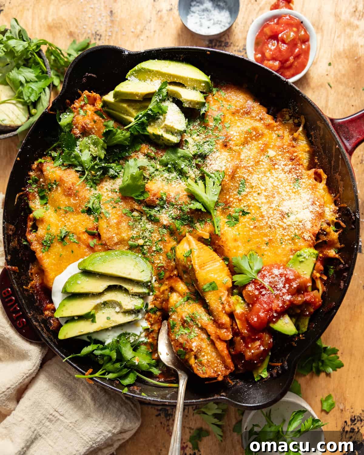 Cast iron skillet of Mexican stuffed shells topped with fresh avocado and onion, glistening and ready for serving.