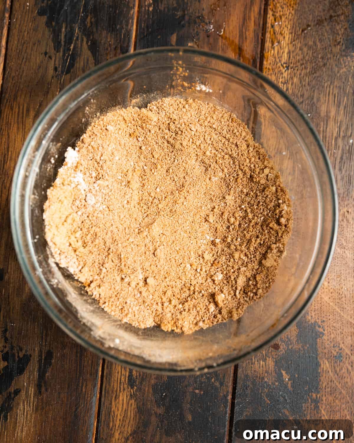 Brown sugar and various spices in a small glass mixing bowl on a wooden table.