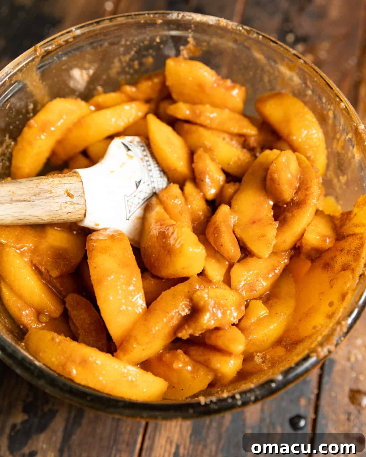 A rubber spatula in a mixing bowl of sugary peach slices.