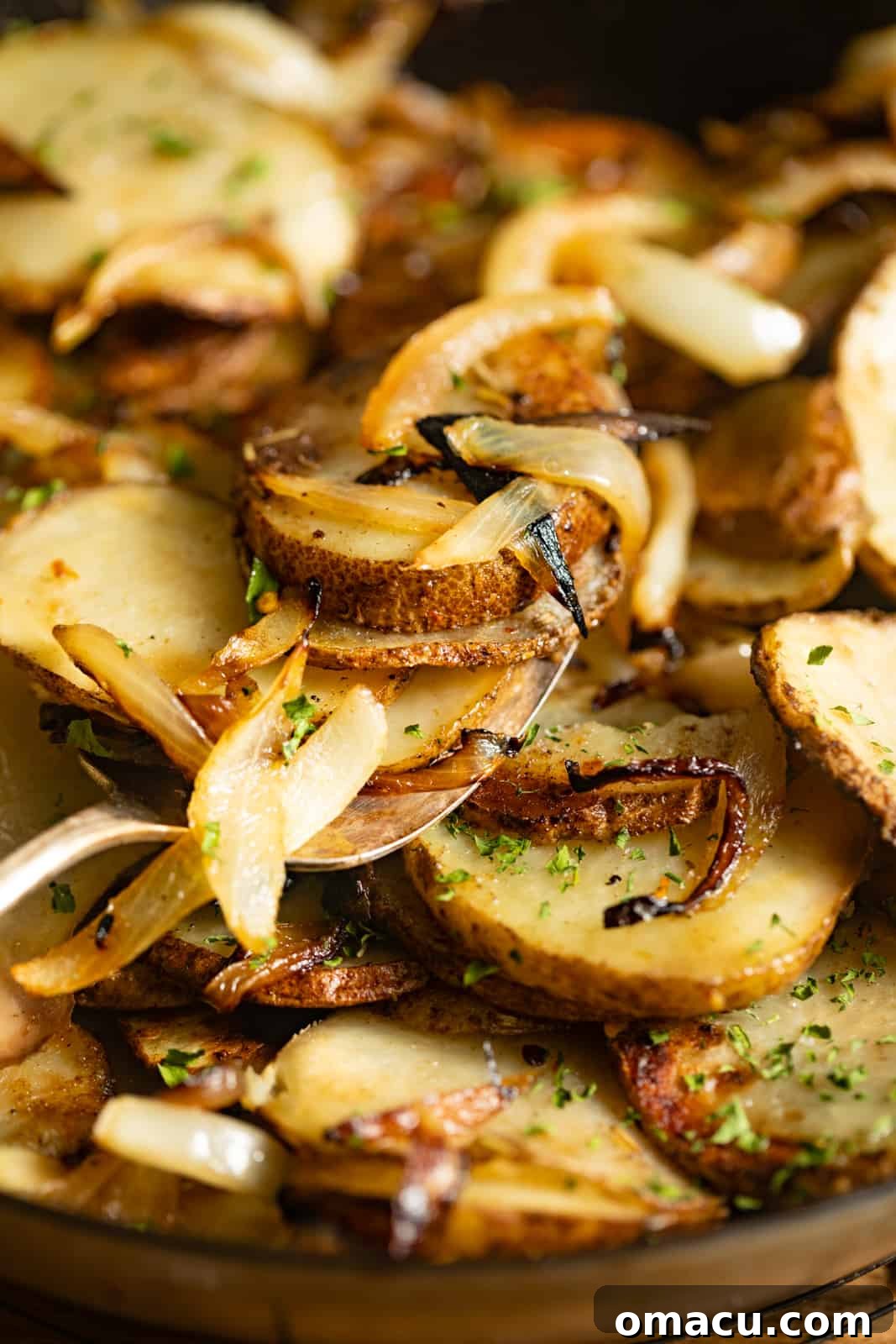 A fork holding a bite of fried potatoes and onions over a full cast iron skillet, showcasing the golden-brown crispiness.