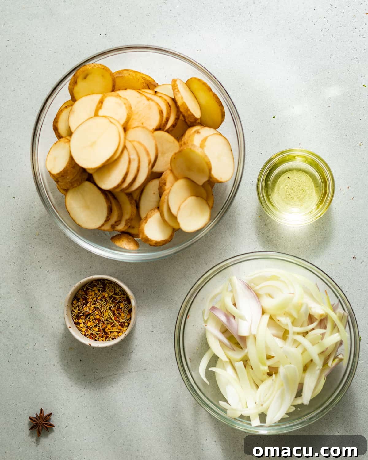 Ingredients to make fried potatoes and onions arranged in small bowls on a clean white surface, highlighting freshness.