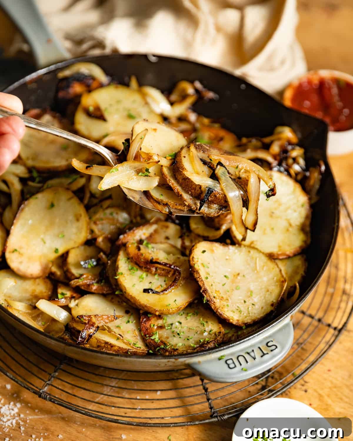 A fork holding a bite of perfectly sliced and fried potatoes over a full cast iron skillet, ready to be enjoyed.