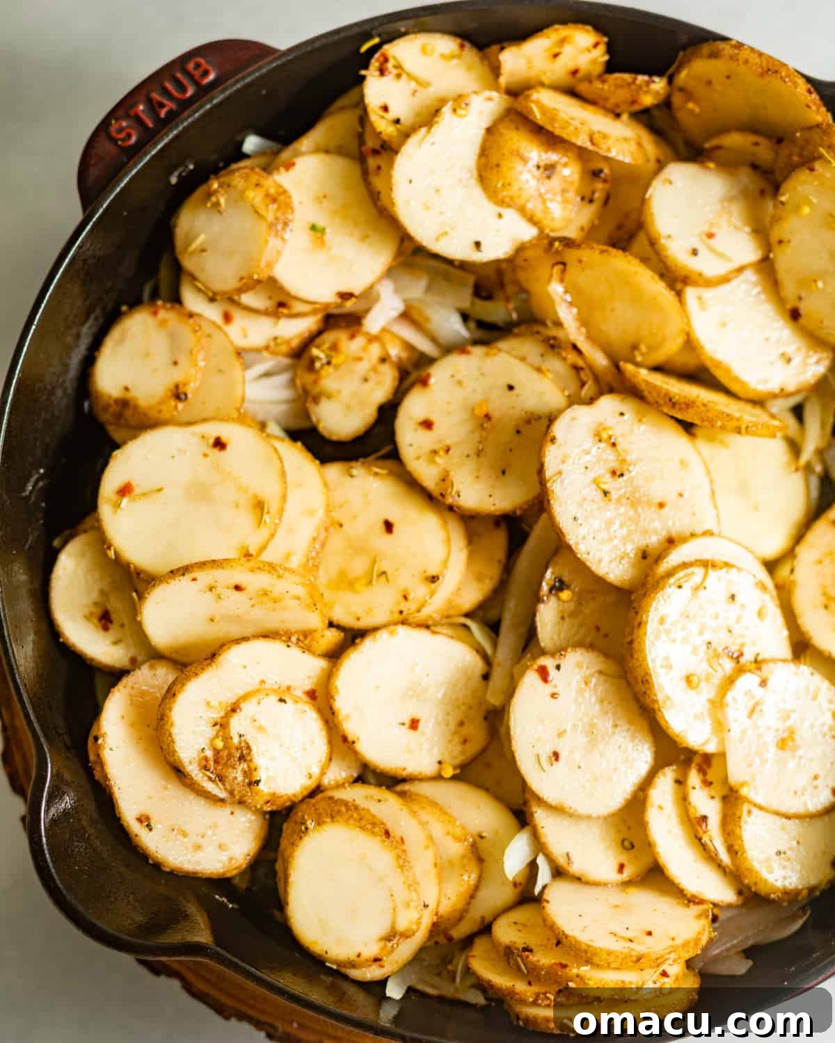 Sliced potatoes with seasonings carefully placed in a cast iron skillet, beginning to sizzle.