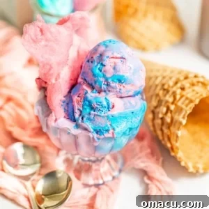 A stunning glass cup filled with swirled pink and blue cotton candy ice cream, garnished with spoons and waffle cones in the background, ready to be devoured.