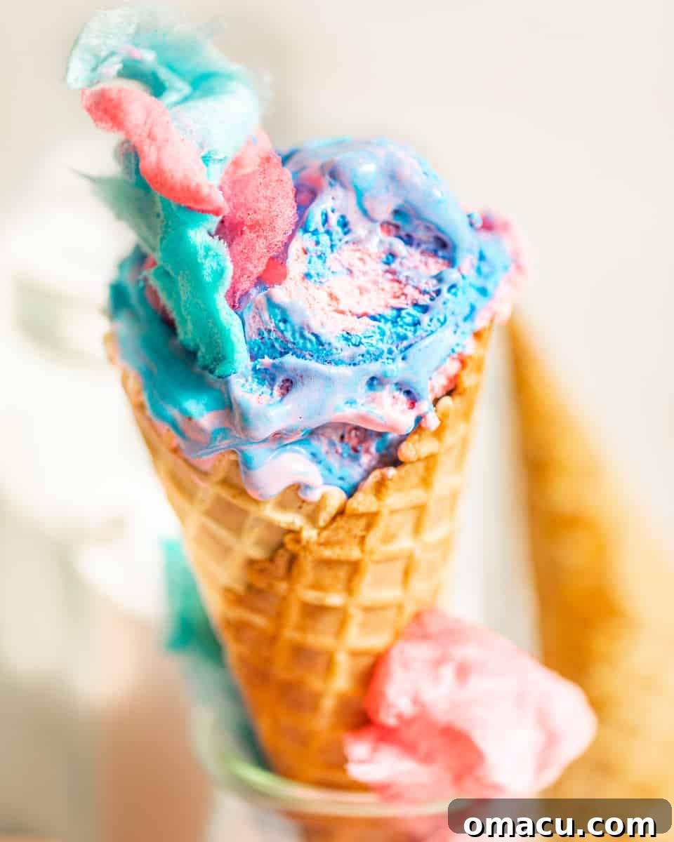 A delectable scoop of vibrant pink and blue cotton candy ice cream, adorned with a cloud of real cotton candy, nestled in a crispy waffle cone, ready to be enjoyed.