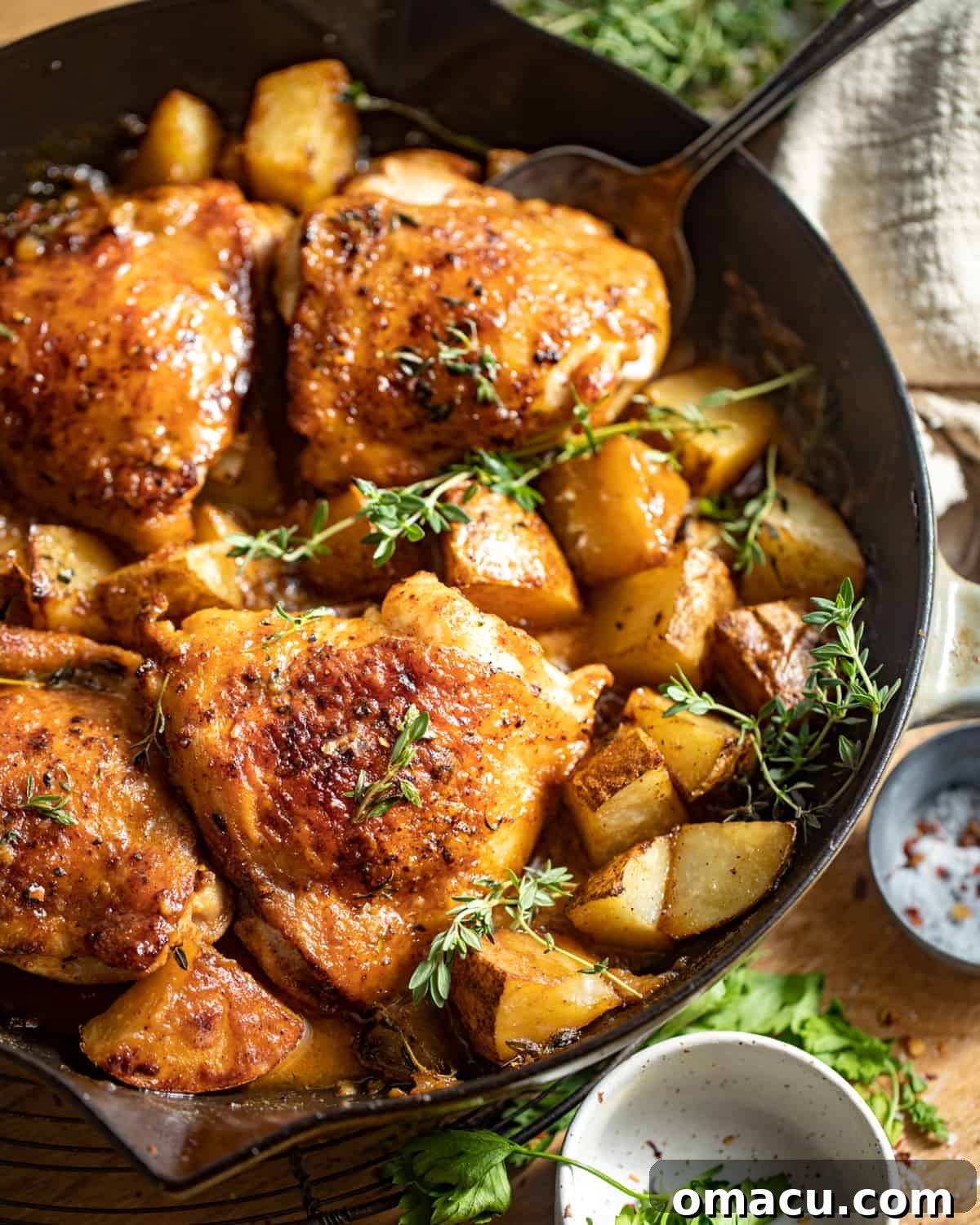 Golden brown maple dijon chicken thighs nestled among roasted creamer potatoes in a rustic cast iron skillet, ready to serve.