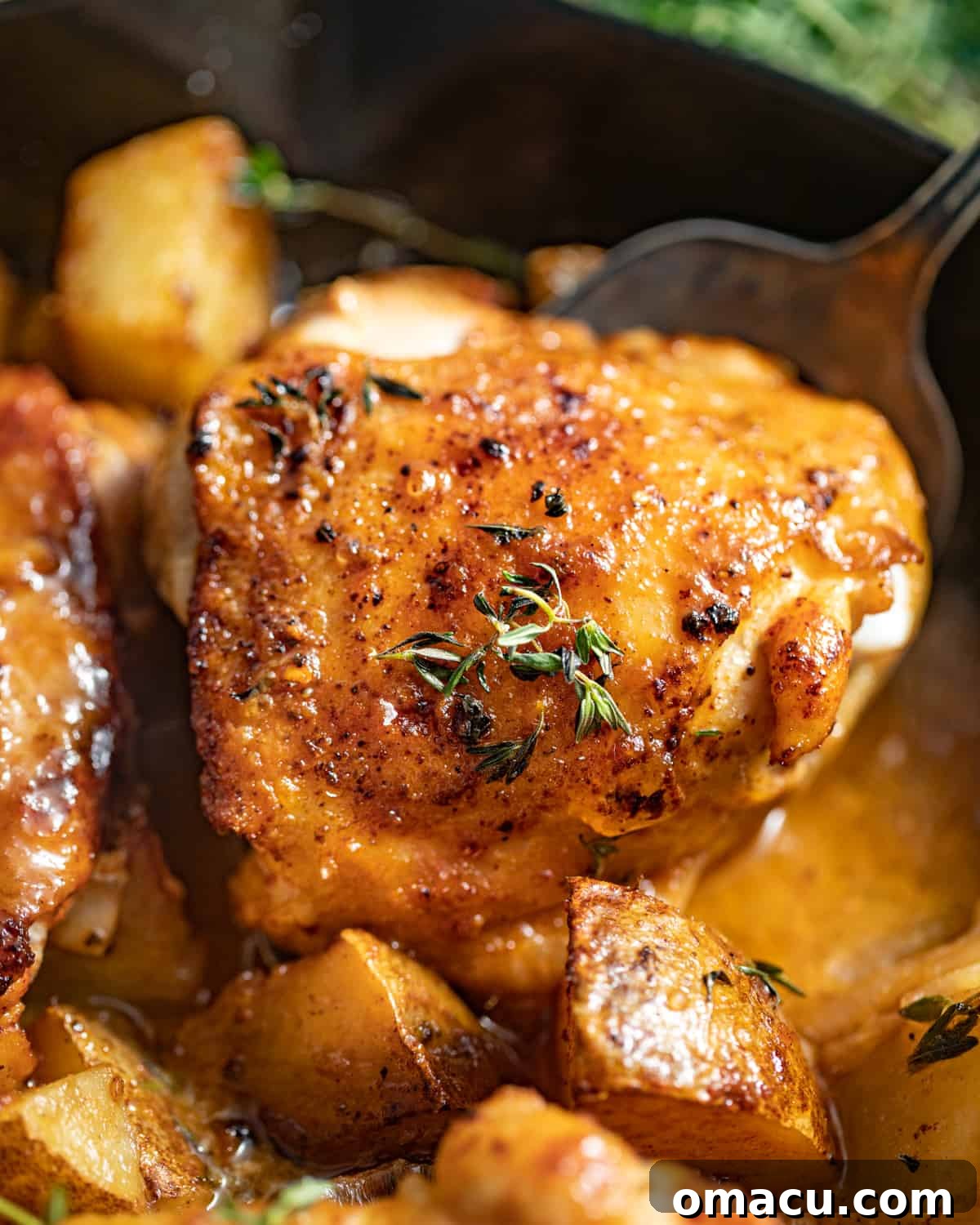A close-up of a spoon scooping up a piece of maple dijon chicken thigh from the skillet, highlighting the creamy sauce and crispy skin.