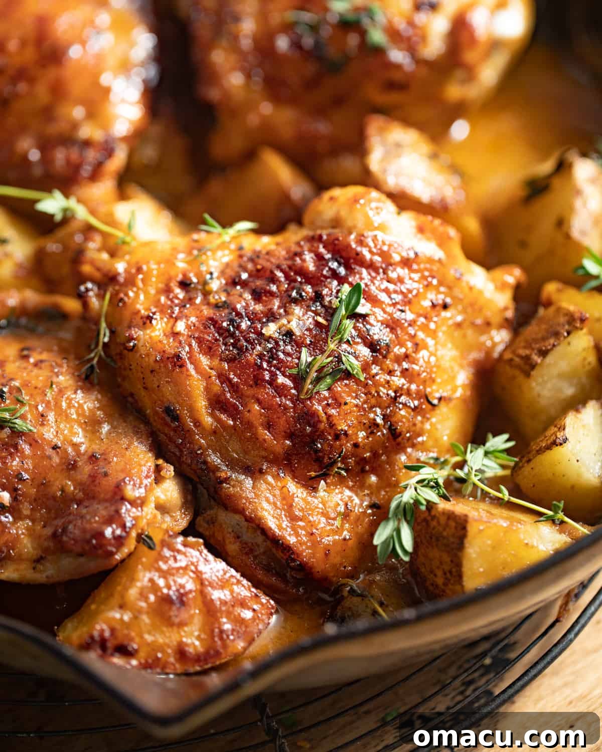 Close-up of the beautifully crispy skin on a maple dijon chicken thigh, with blurred tender potatoes in the background.