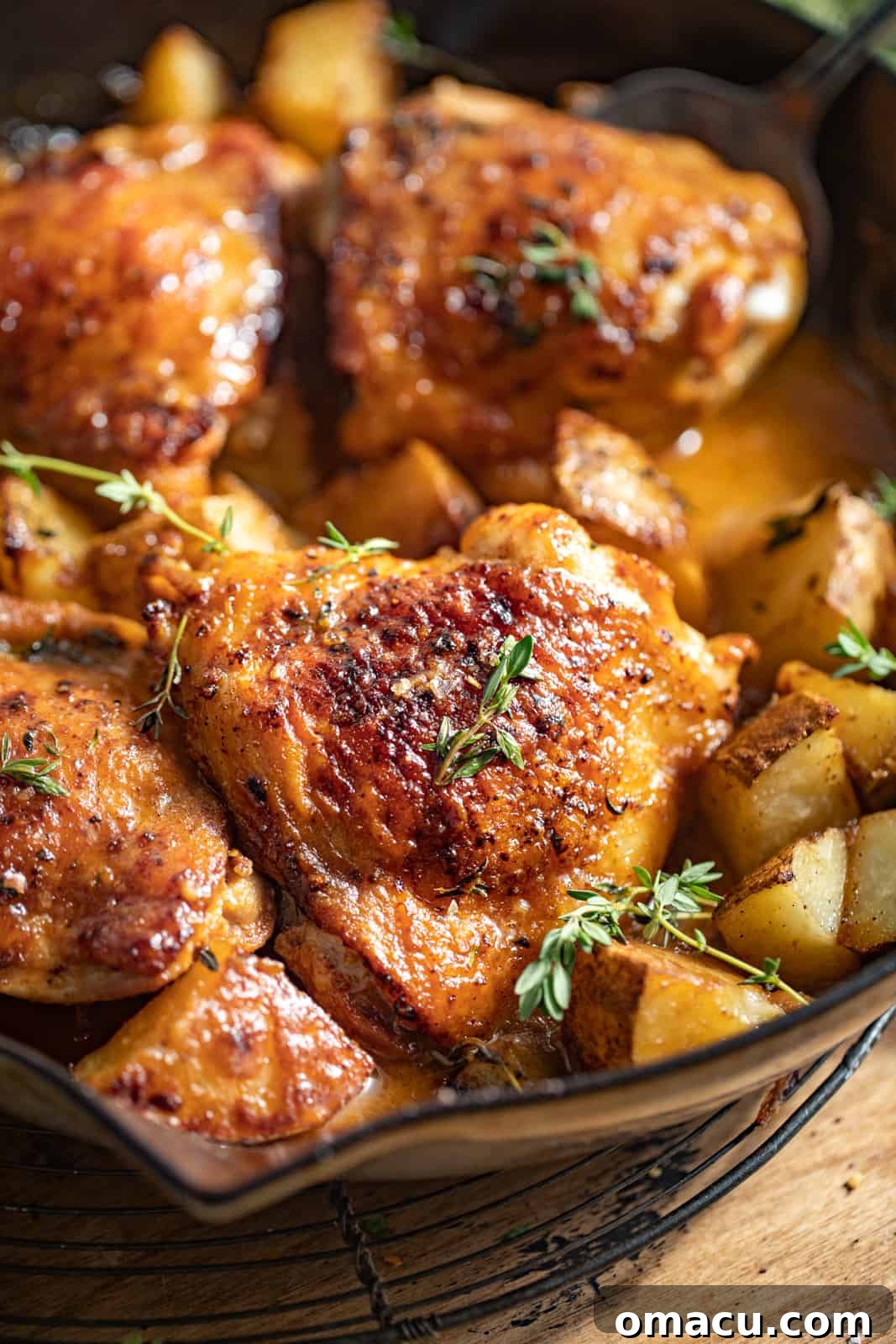 A top-down shot of the finished maple dijon chicken thighs and potatoes in the cast iron skillet, garnished with fresh thyme.