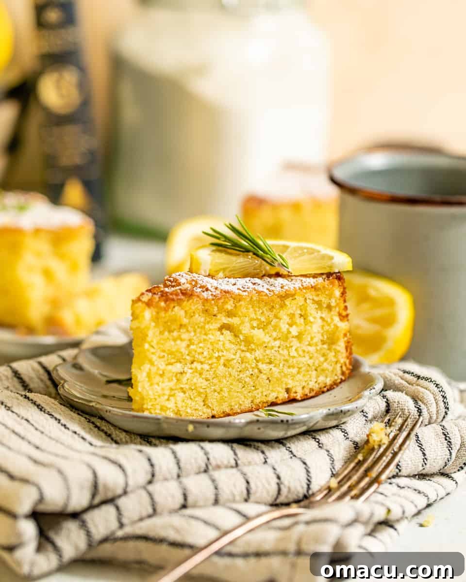 A perfectly golden slice of Lemon Rosemary Olive Oil Cake on a small white plate, resting on a textured kitchen towel, inviting a delightful first bite.