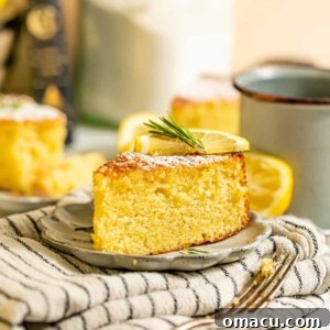 A perfectly golden slice of Lemon Rosemary Olive Oil Cake on a small white plate, resting on a textured kitchen towel, inviting a delightful first bite.