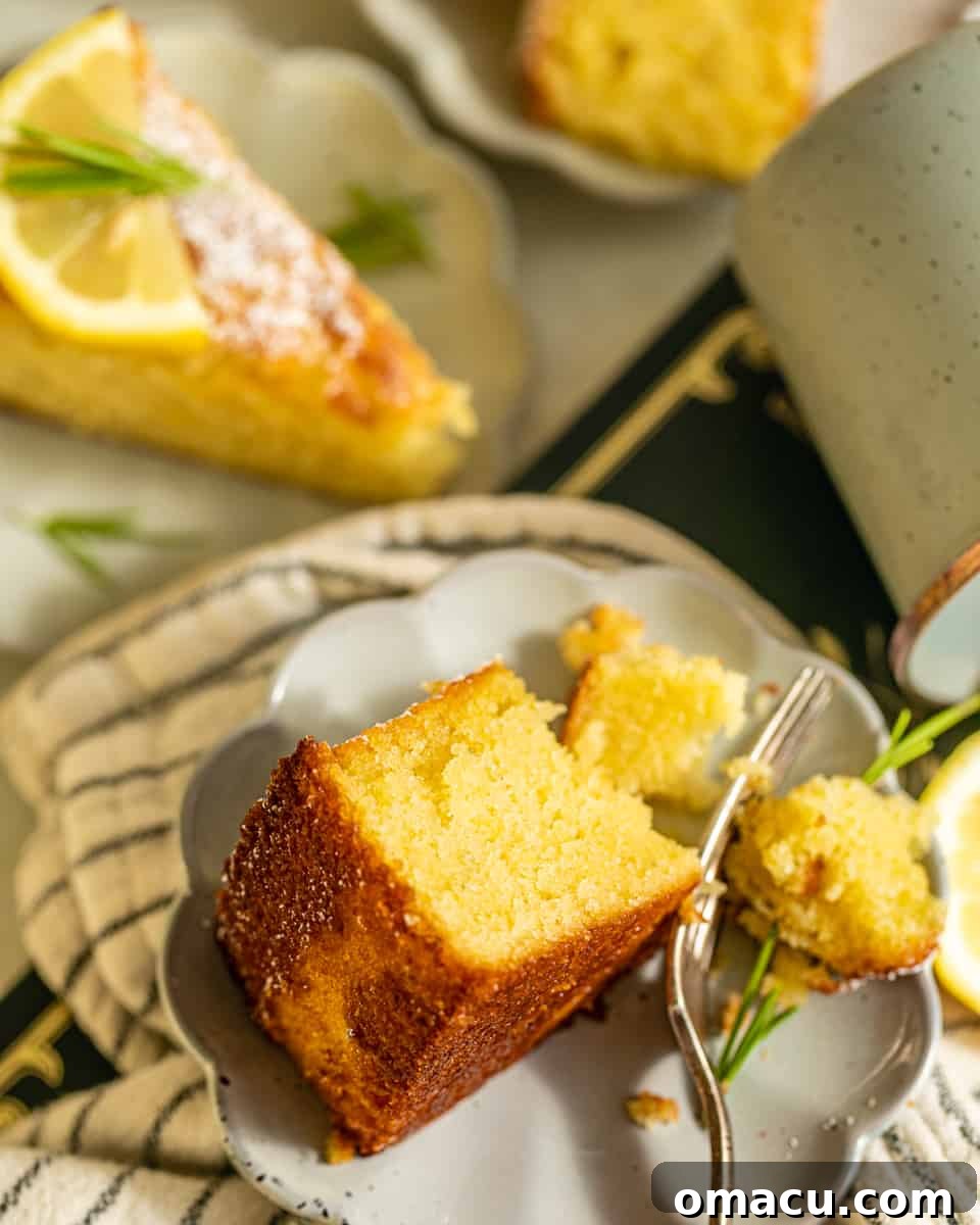 A delectable slice of Lemon Rosemary Olive Oil Cake presented on a small white plate with a fork, ready to be enjoyed.