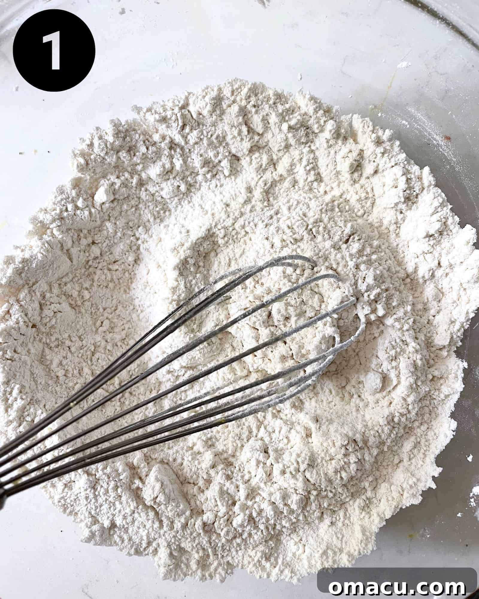 All-purpose flour, ground ginger, baking powder, baking soda, and kosher salt are whisked together in a mixing bowl, creating the base for the dry ingredients.
