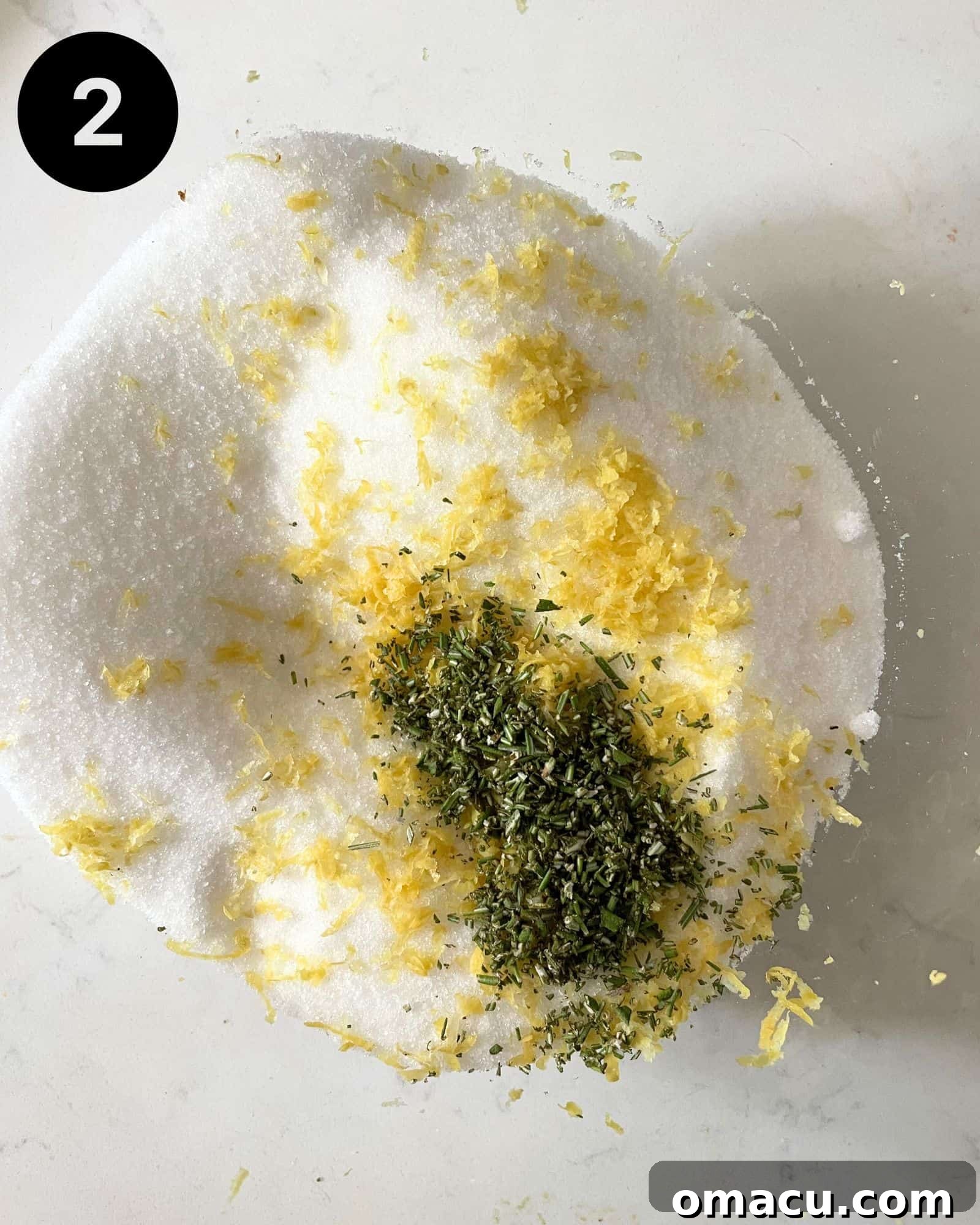 Granulated sugar, fresh rosemary, and lemon zest are combined in a mixing bowl, being rubbed together to infuse aromatic oils.