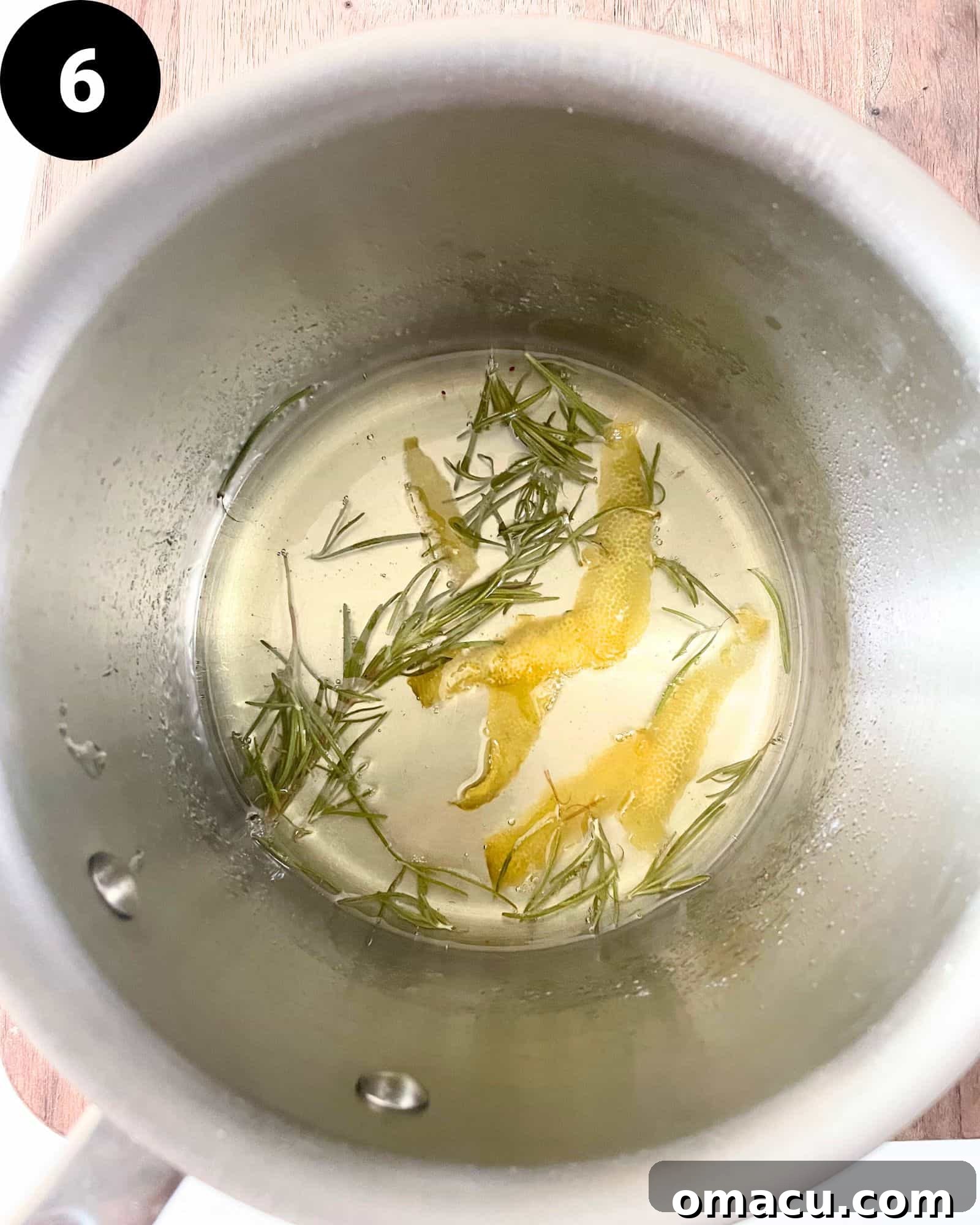 A simmering rosemary lemon simple syrup in a saucepan, infusing with fragrant herbs and citrus peels.