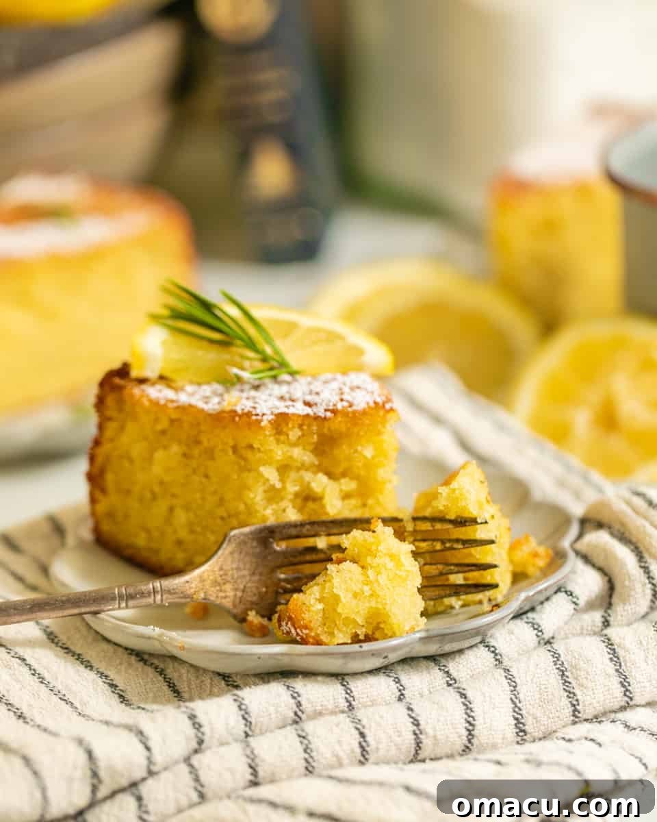 A slice removed from a whole Lemon Rosemary Olive Oil Cake on a plate, showcasing its moist texture and golden crust.