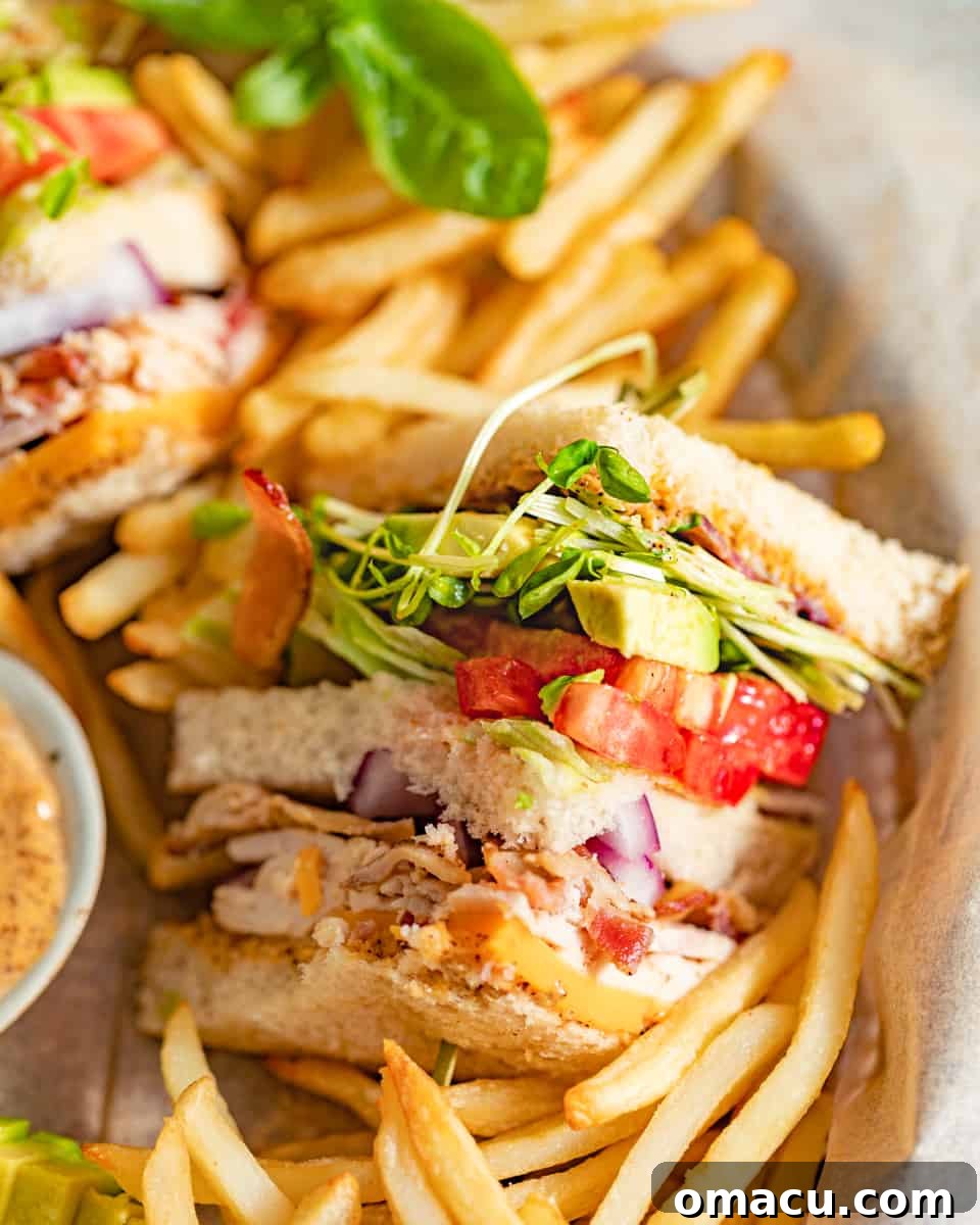 A California Club Sandwich cut into a perfect triangle, resting on a plate next to a pile of crispy french fries.