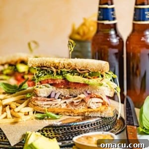 A club sandwich cut in half with french fries and chipotle mayo in a bowl.