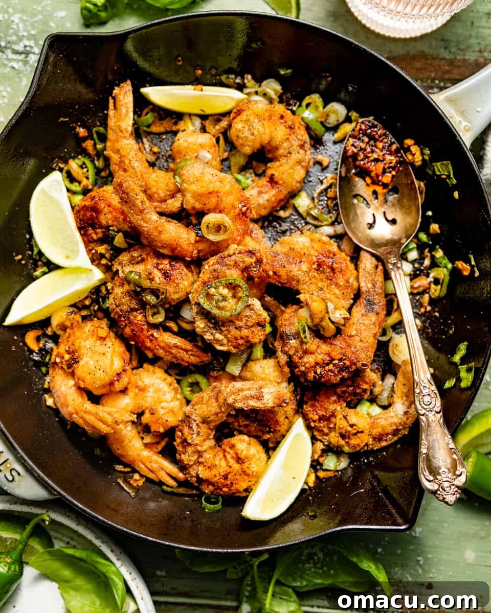 Salt and Pepper Shrimp served in a skillet with a serving spoon, garnished with fresh green onions for a pop of color and freshness.