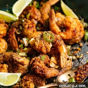 Salt and Pepper Shrimp in a large skillet with fresh limes, highlighting the golden-fried seafood.