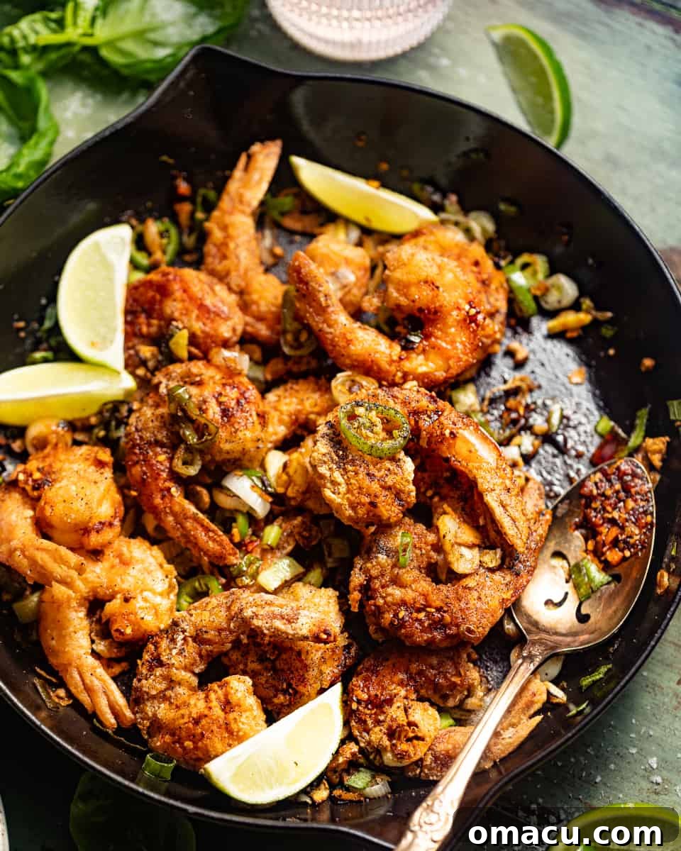 Salt and Pepper Shrimp served in a large skillet, adorned with fresh lime slices and a drizzle of chili crunch for added flavor and visual appeal.