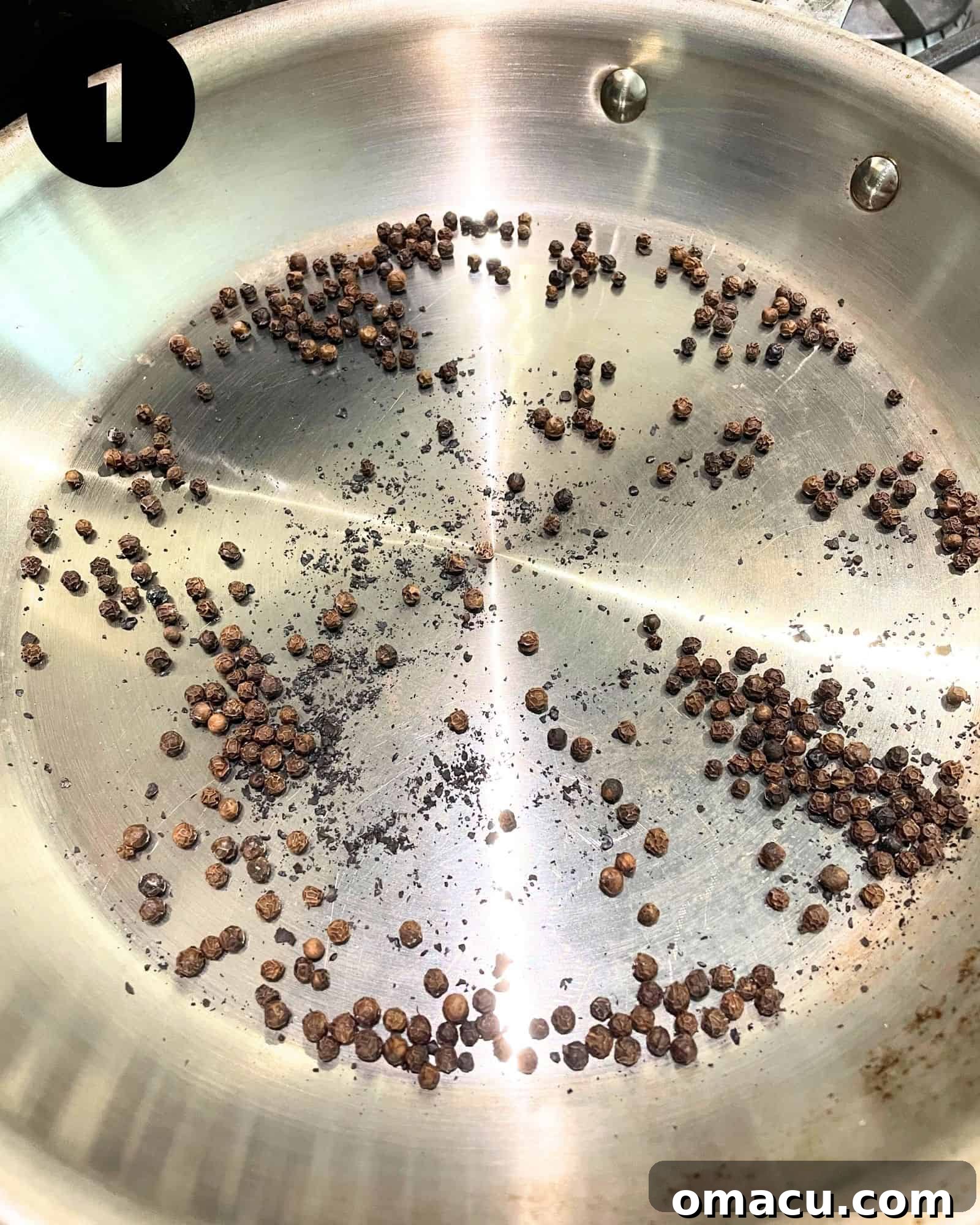 Whole black peppercorns lightly toasting in a dry skillet over gentle heat, releasing their aromatic oils.