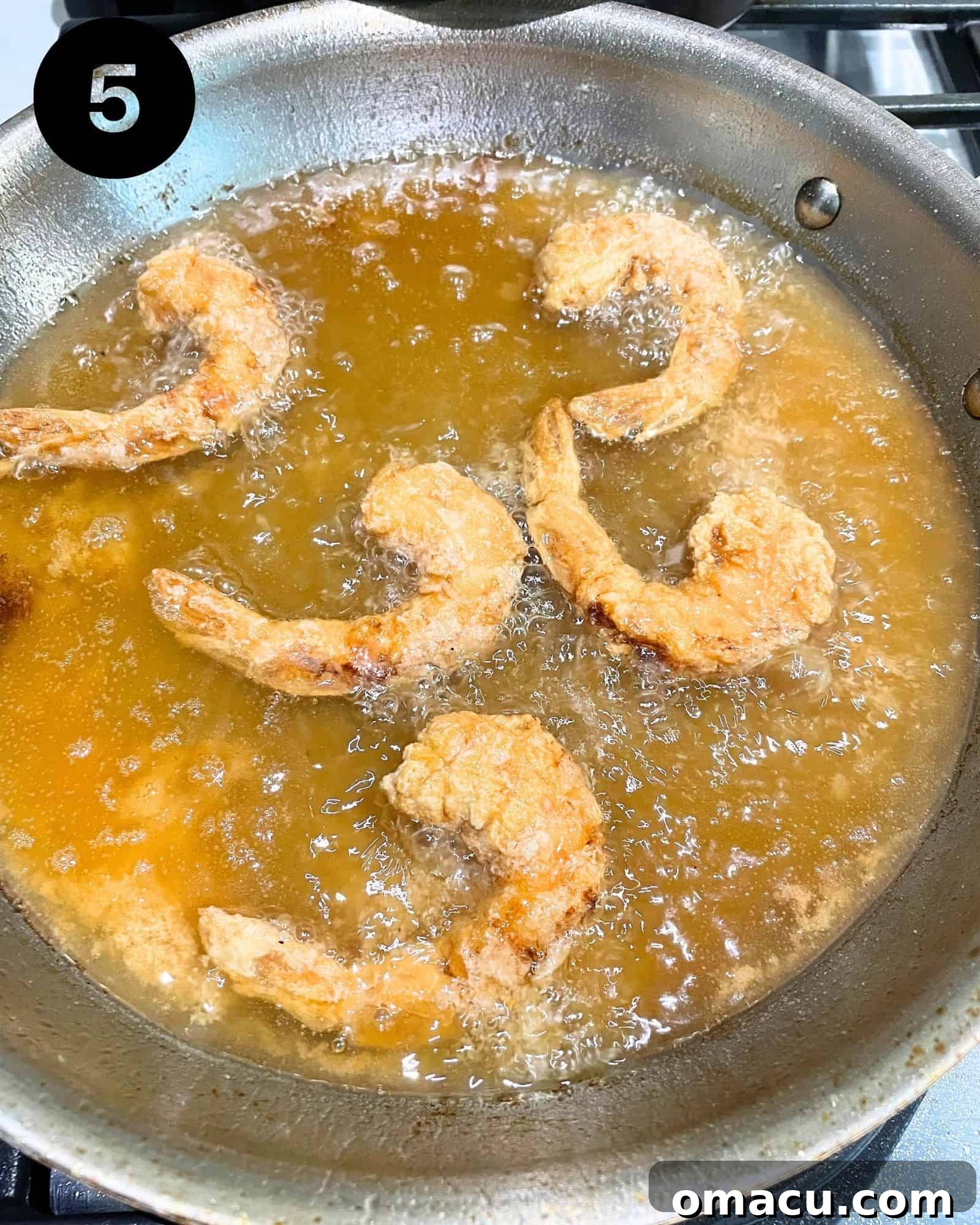 Golden brown, crispy fried shrimp being carefully removed from the skillet, glistening with oil.