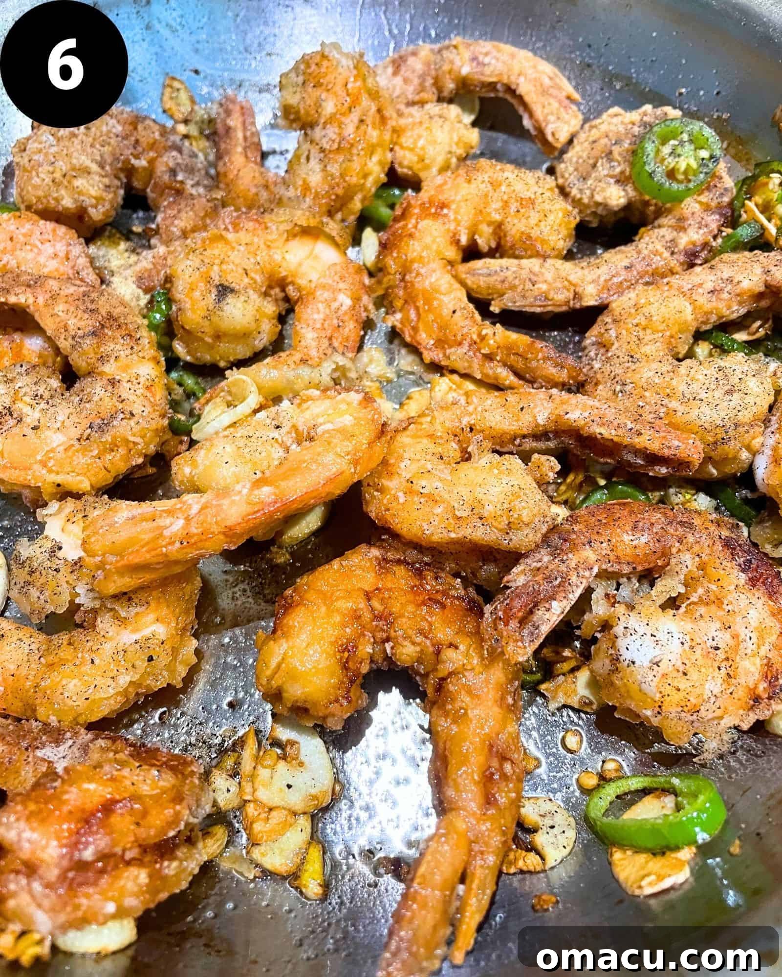 Salt and Pepper Shrimp in a skillet, tossed with sautéed serrano peppers, ginger, and garlic, awaiting the final seasoning sprinkle.