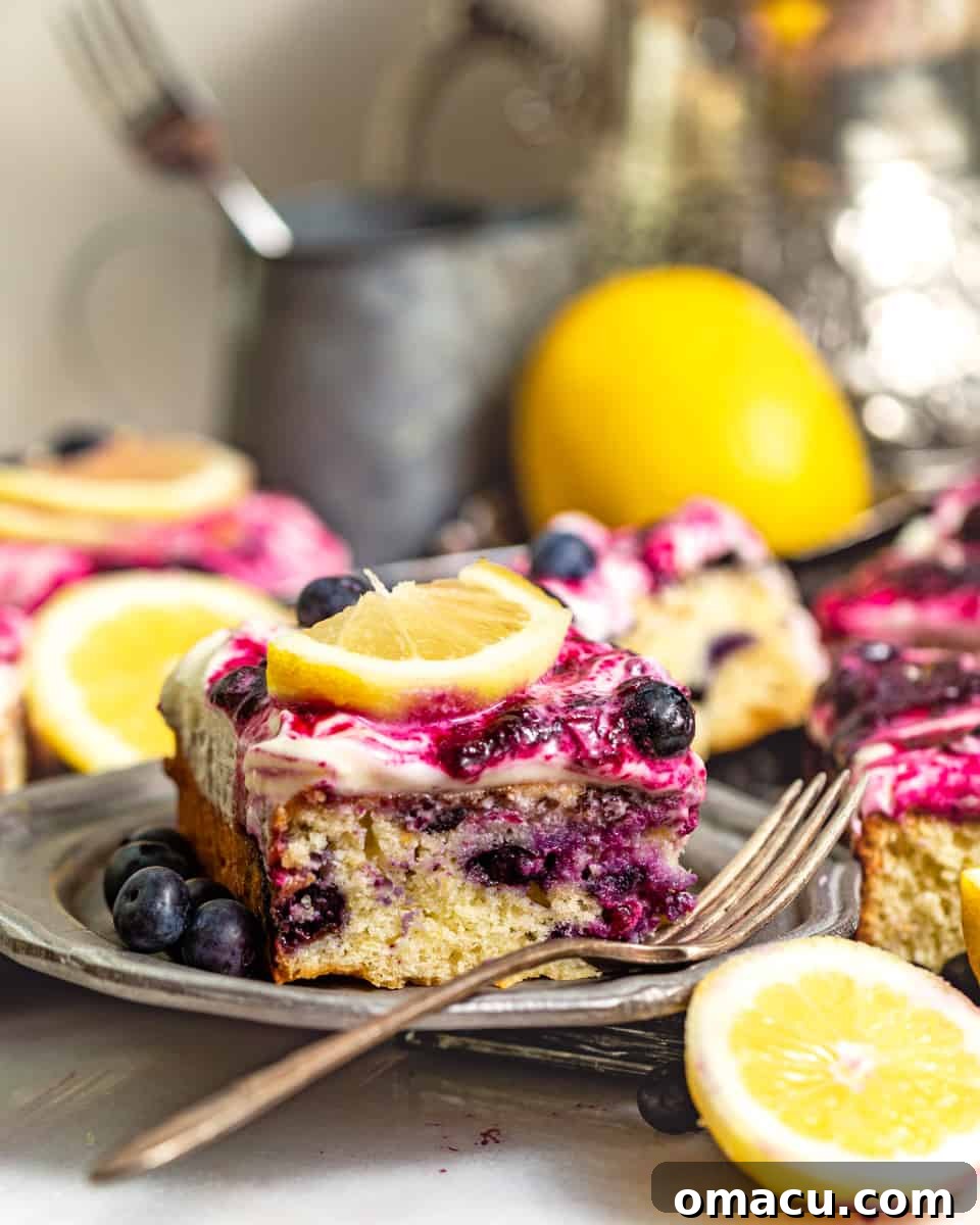 A beautifully sliced piece of lemon blueberry sheet cake on a silver plate with a fork, showing its moist layers and generous frosting.