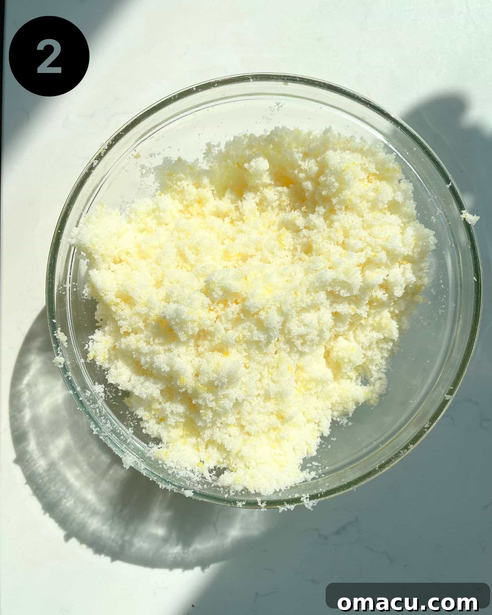 Lemon zest and sugar being rubbed together in a mixing bowl to release citrus aromas.