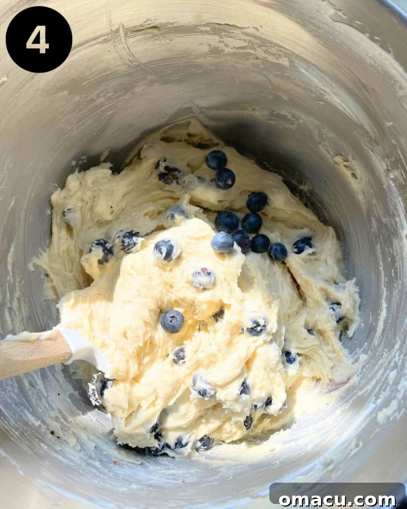 Close-up of fluffy cake batter in a mixing bowl, with fresh blueberries being gently folded in.