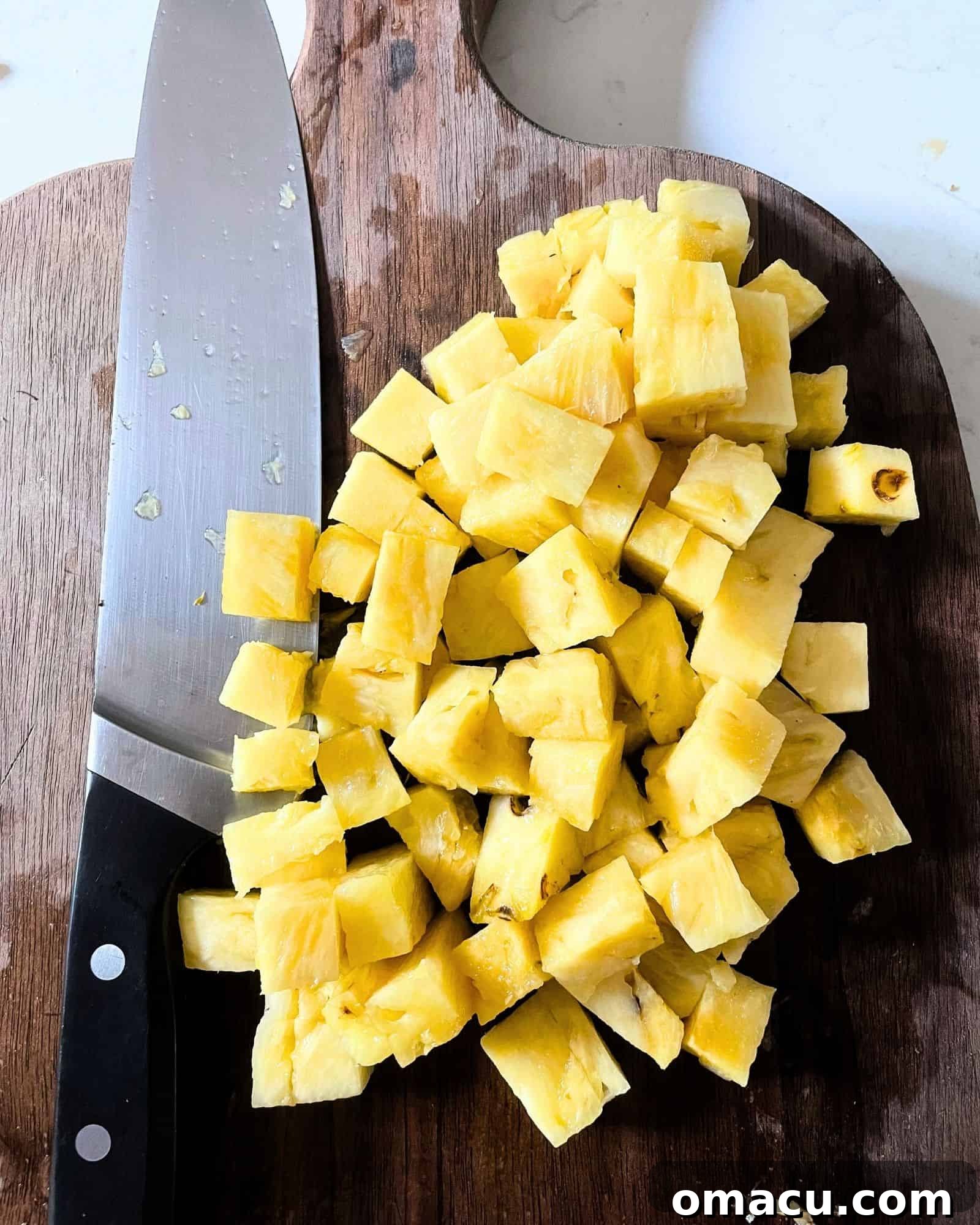A cutting board with perfectly diced pineapple chunks next to a sharp chef's knife, demonstrating the prepared fruit for the salsa.
