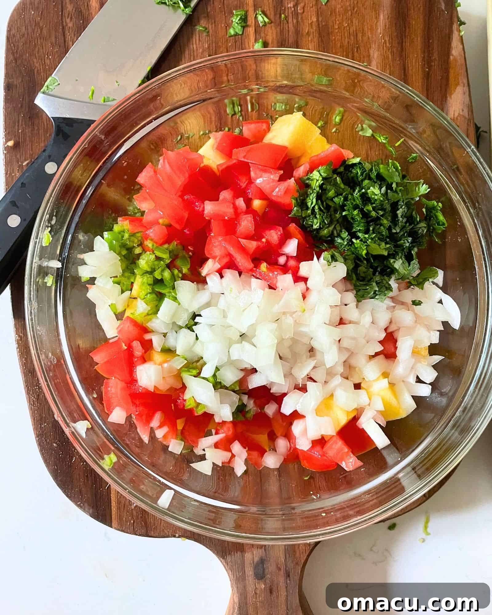 A large mixing bowl filled with vibrant, freshly diced ingredients including tomatoes, cilantro, onion, pineapple, lime zest, and garlic, ready to be combined for pico de gallo.