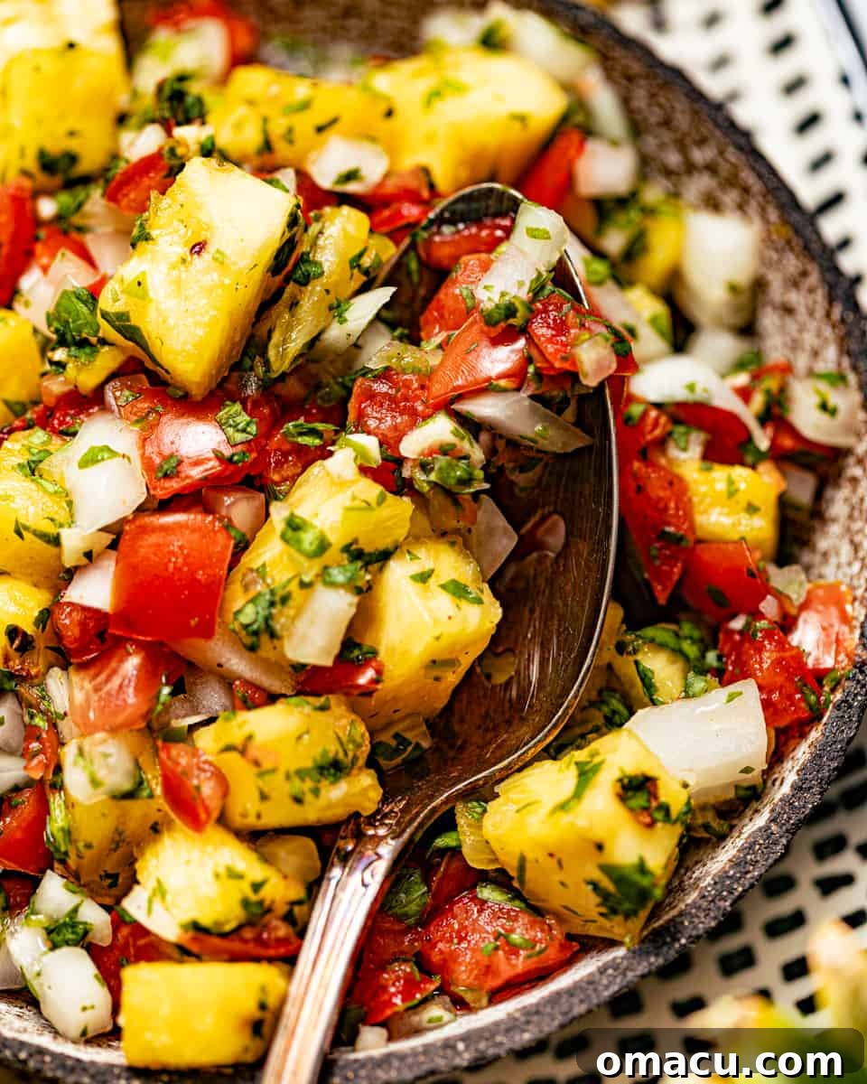 A close-up view of vibrant pineapple pico de gallo in a rustic bowl, with a silver spoon resting inside, highlighting its fresh texture and appeal.