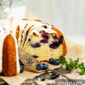 A blueberry pound cake on a wire rack with a piece of parchment paper topped with a cream cheese vanilla glaze.
