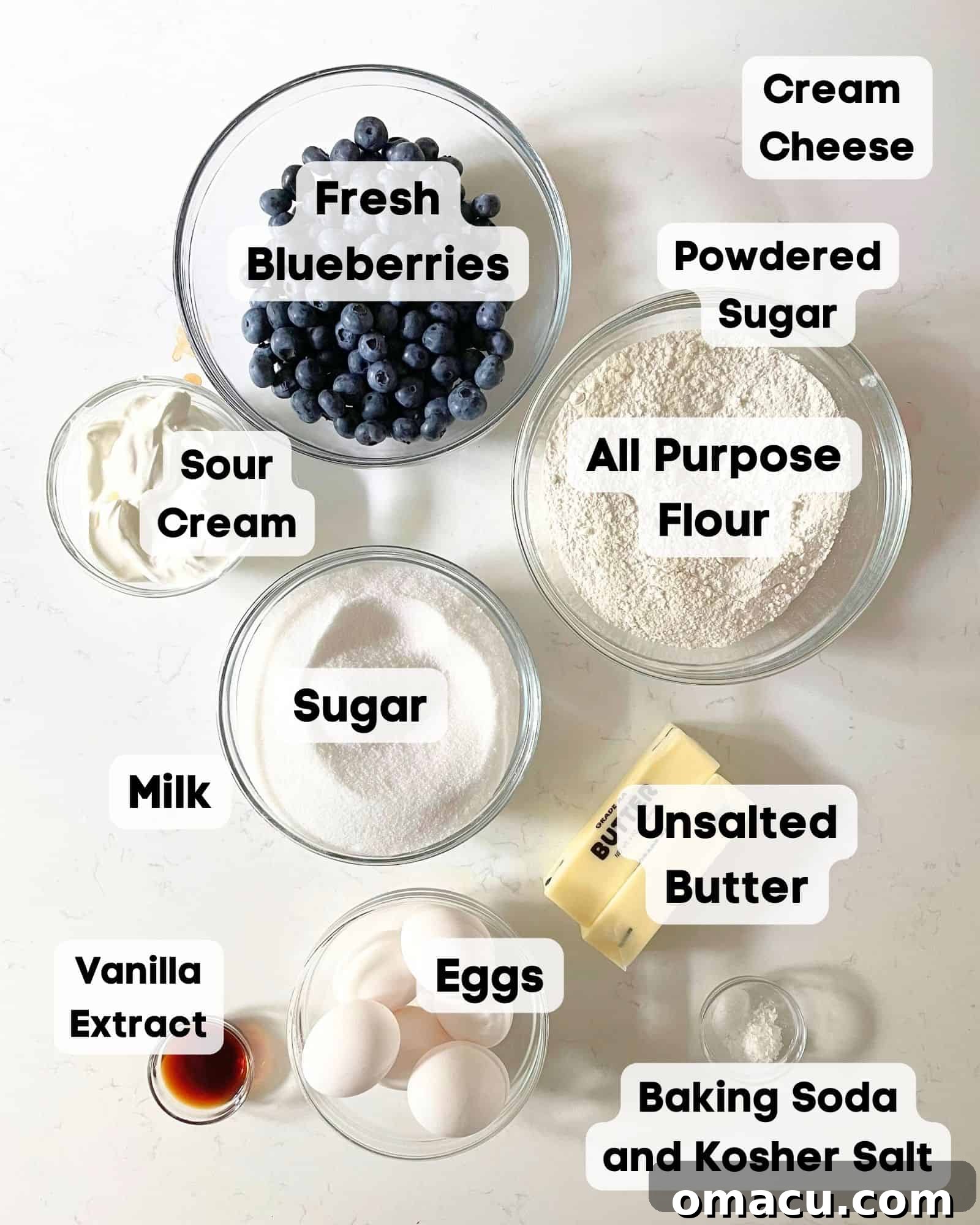 Ingredients laid out for blueberry pound cake: flour, sugar, butter, eggs, vanilla extract, baking soda, salt, blueberries, and sour cream.
