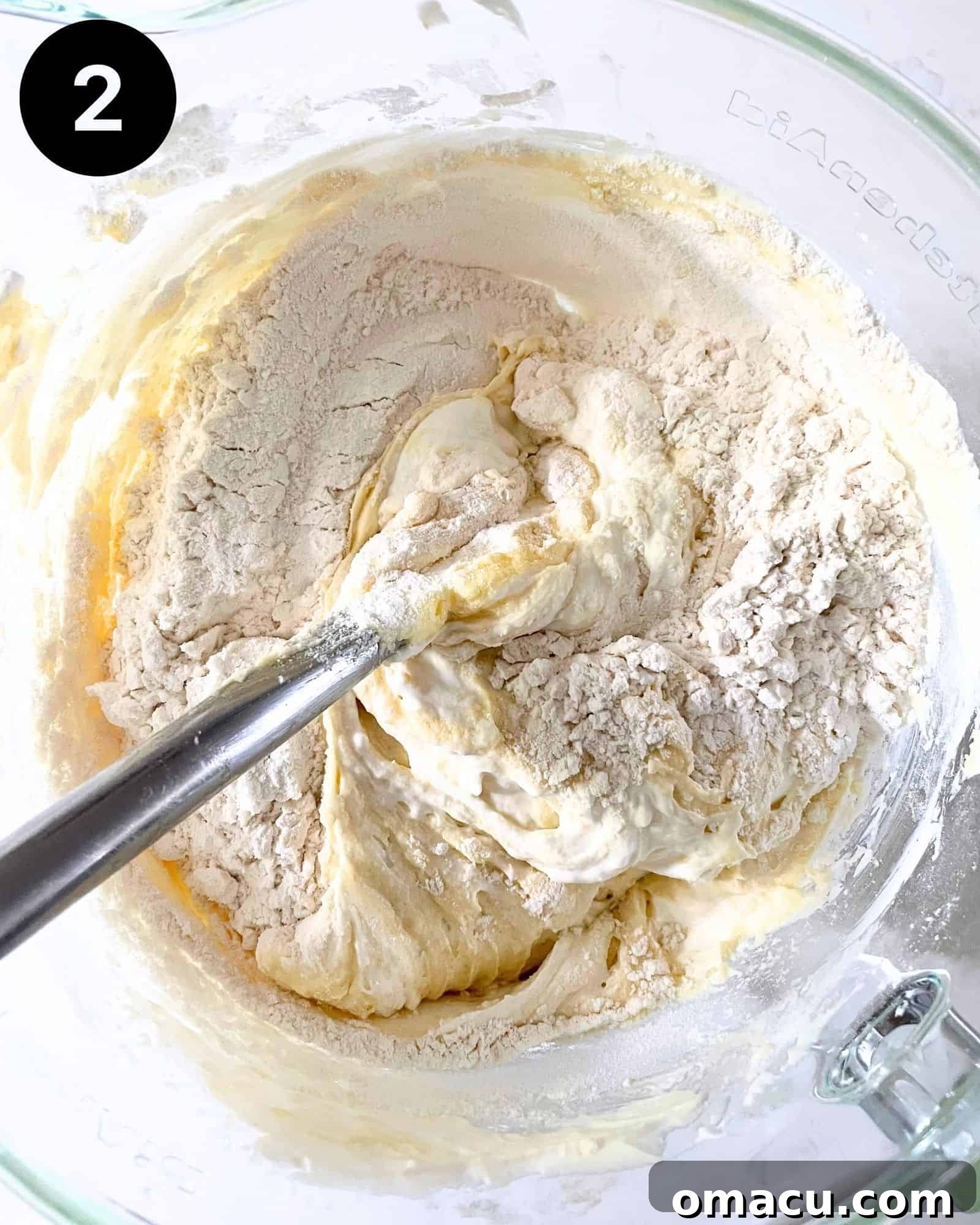 Cake batter in a bowl with dry ingredients partially mixed in, showing a smooth consistency.
