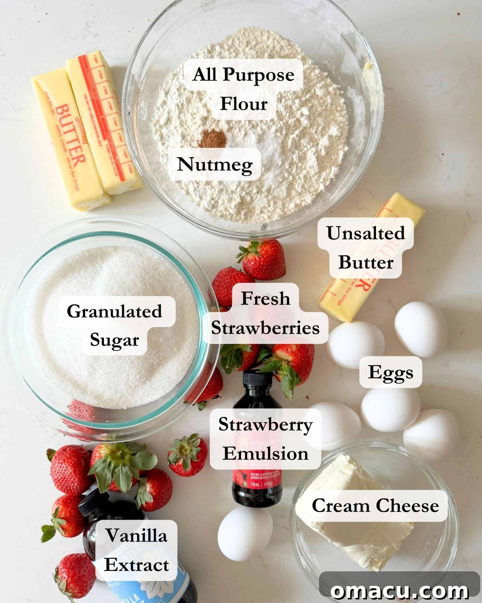 A selection of fresh ingredients for strawberry pound cake arranged on a white counter, including all-purpose flour, vibrant fresh strawberries, eggs, unsalted butter, nutmeg, strawberry emulsion, vanilla extract, cream cheese, and granulated sugar.