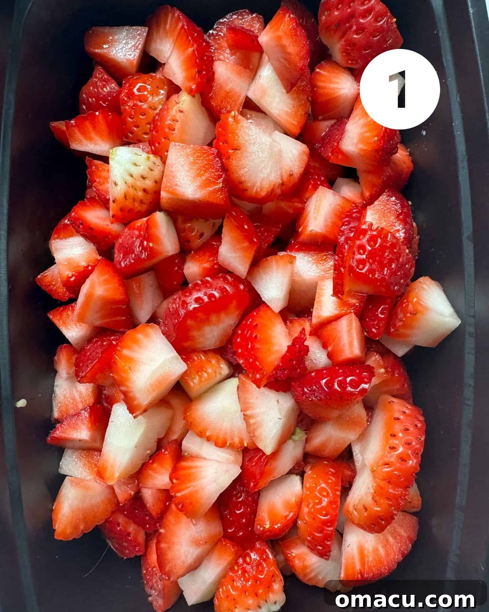 Fresh strawberries expertly cut into uniform chunks, resting in a sleek black bowl, ready for baking.