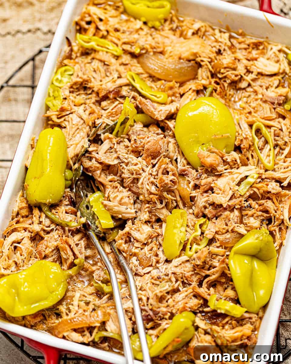 mississippi chicken in a baking pan with a spoon garnished with pepperoncini peppers.
