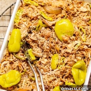 mississippi chicken in a baking pan with a spoon garnished with pepperoncini peppers.