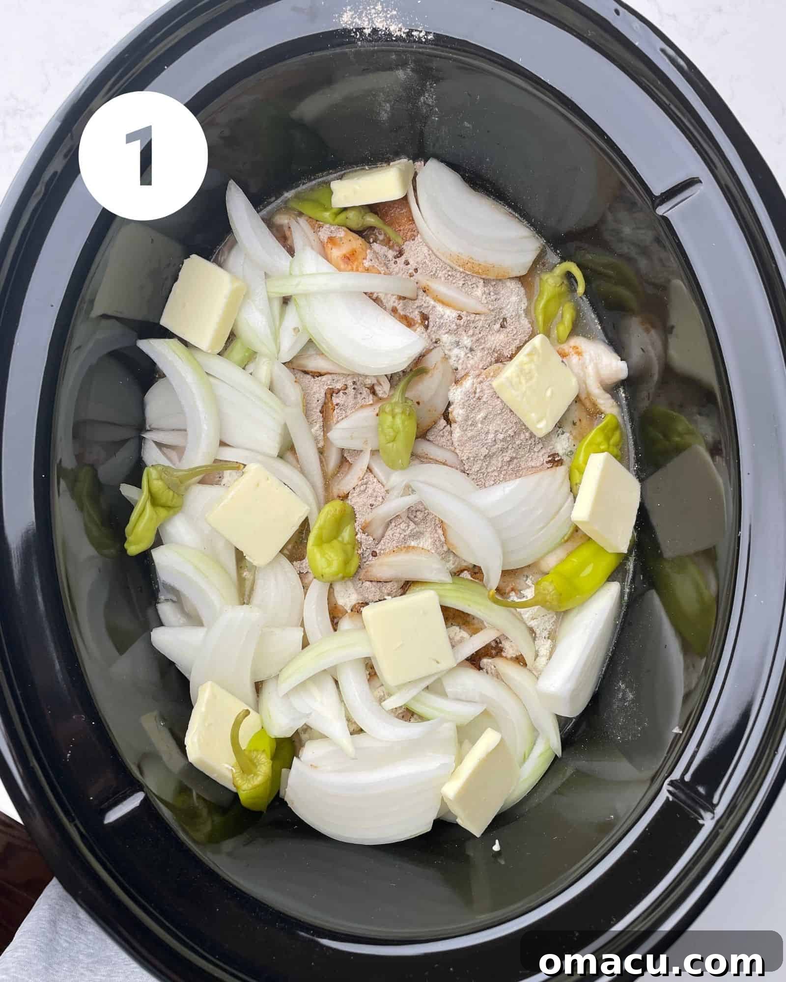 chicken in a slow cooker topped with butter, broth, ppperoncini peppers, onion, and seasoning packets.