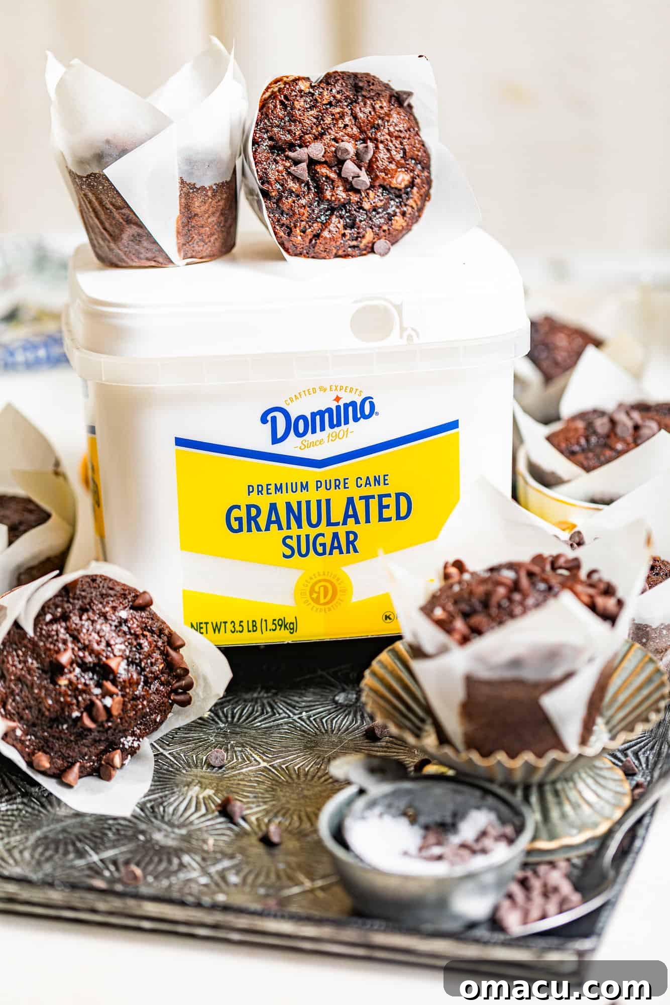 Two perfectly baked brownie muffins resting on top of a tub of Domino® Sugar, with natural light highlighting their texture.