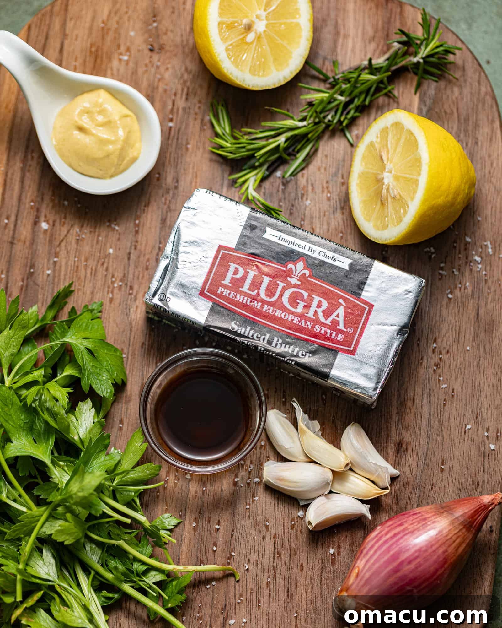 Ingredients laid out on a table to make steak butter, including butter, lemon, rosemary, parsley, garlic, shallots, dijon mustard, and worcestershire sauce.