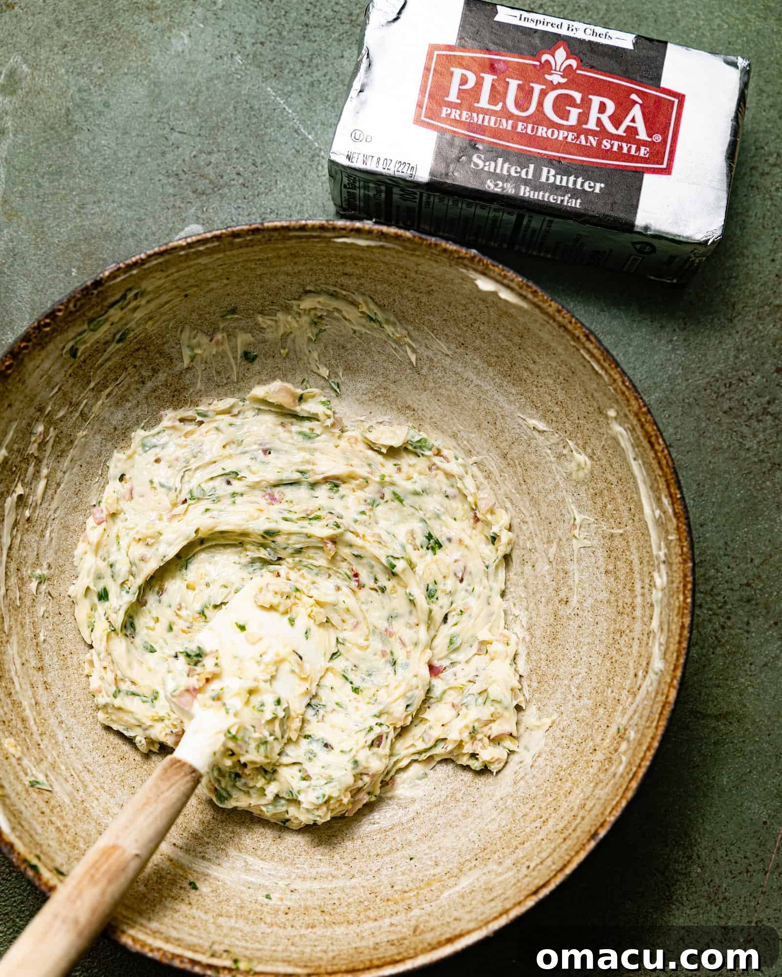Compound butter in a bowl with a spoon, showcasing its creamy texture and visible herb specks.