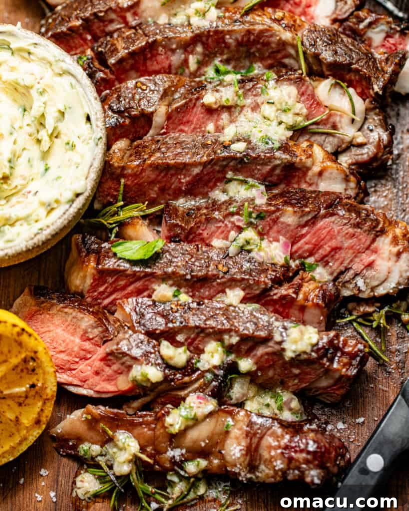 Sliced steak on a cutting board, garnished with fresh herbs, alongside a bowl of steak butter.