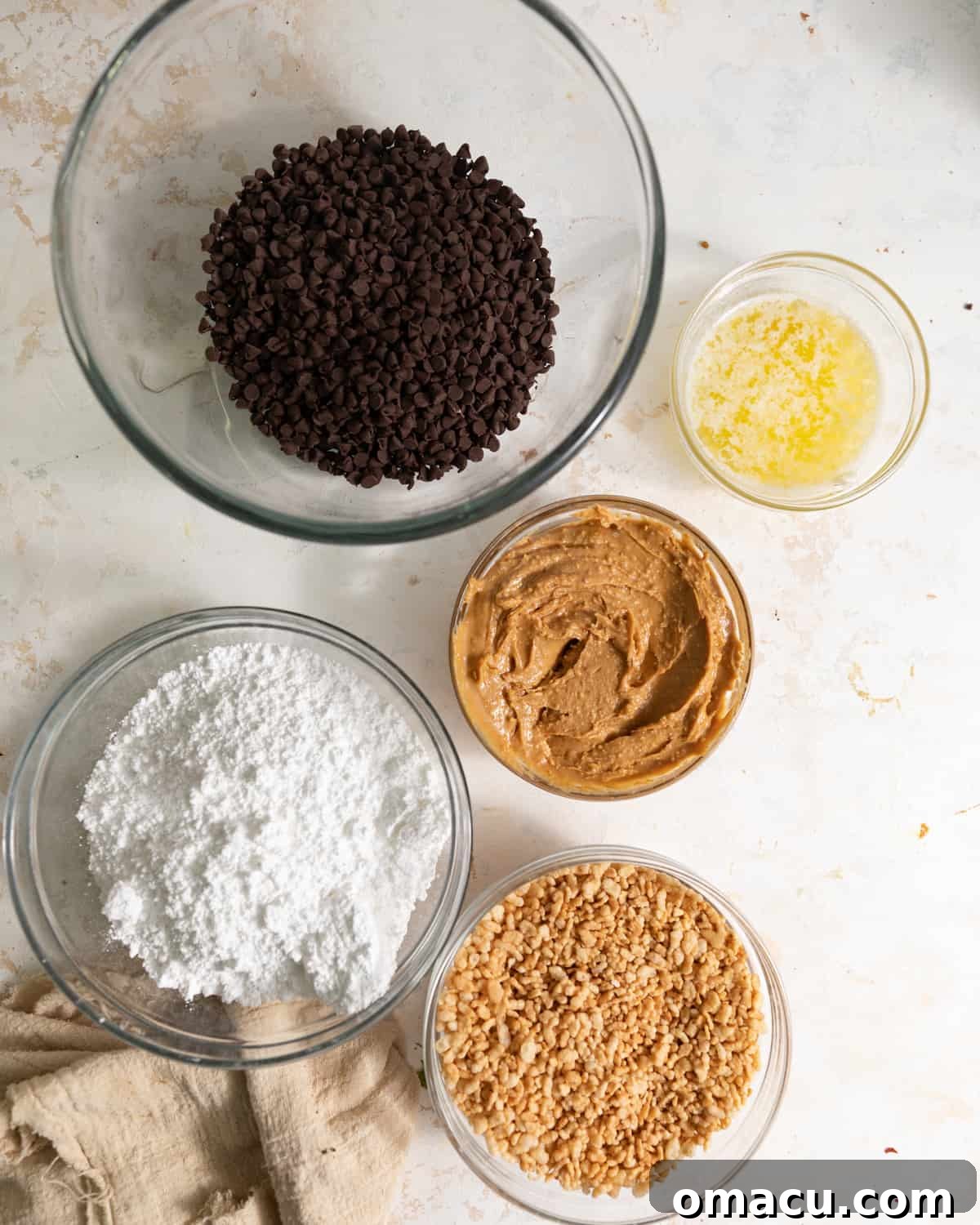 Ingredients to make peanut butter truffles in bowls on a counter. Melted butter, chocolate chips, peanut butter, powdered sugar, rice krispies cereal, and vanilla extract.