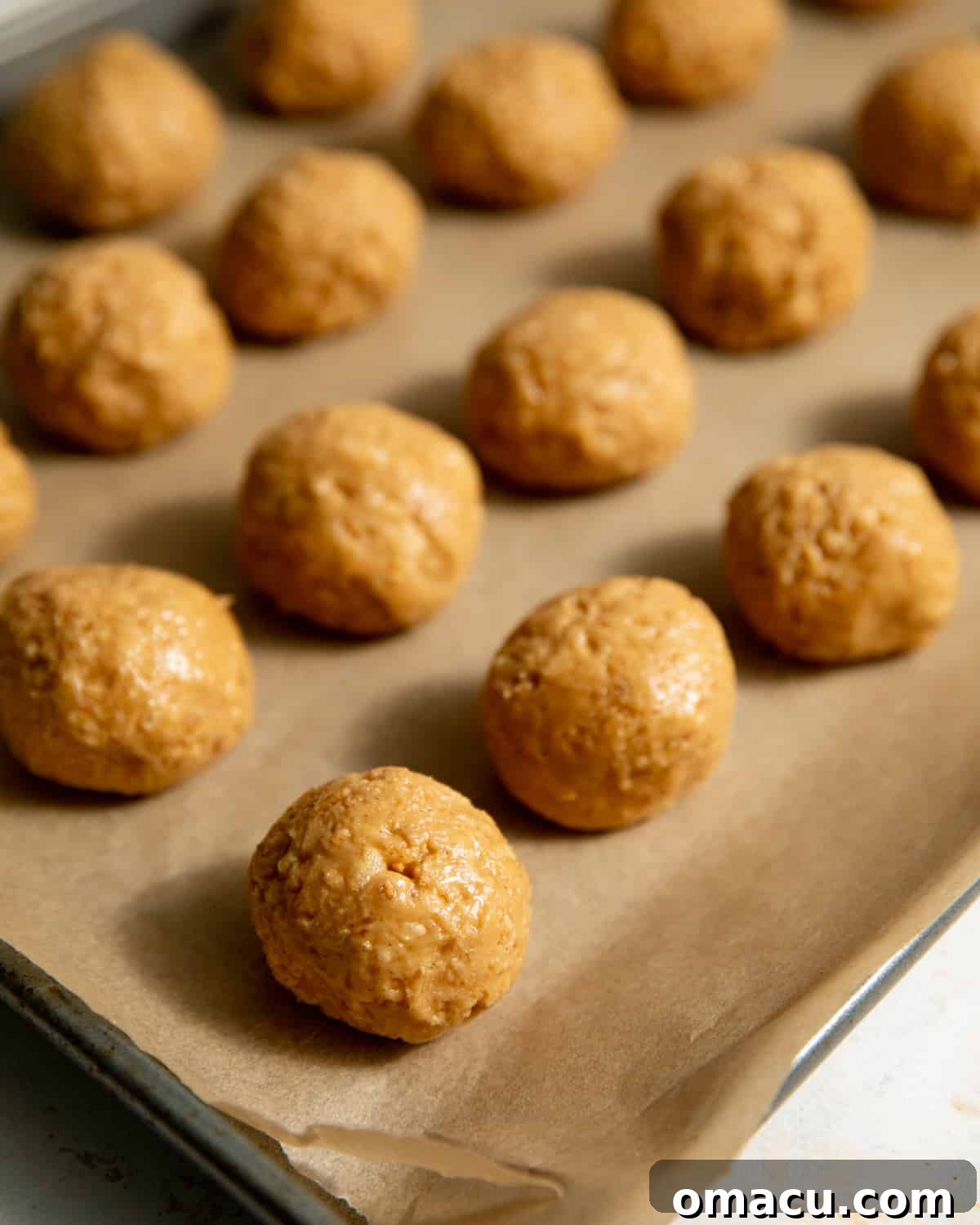 Peanut butter truffle filling in balls on a parchment lined sheet pan.