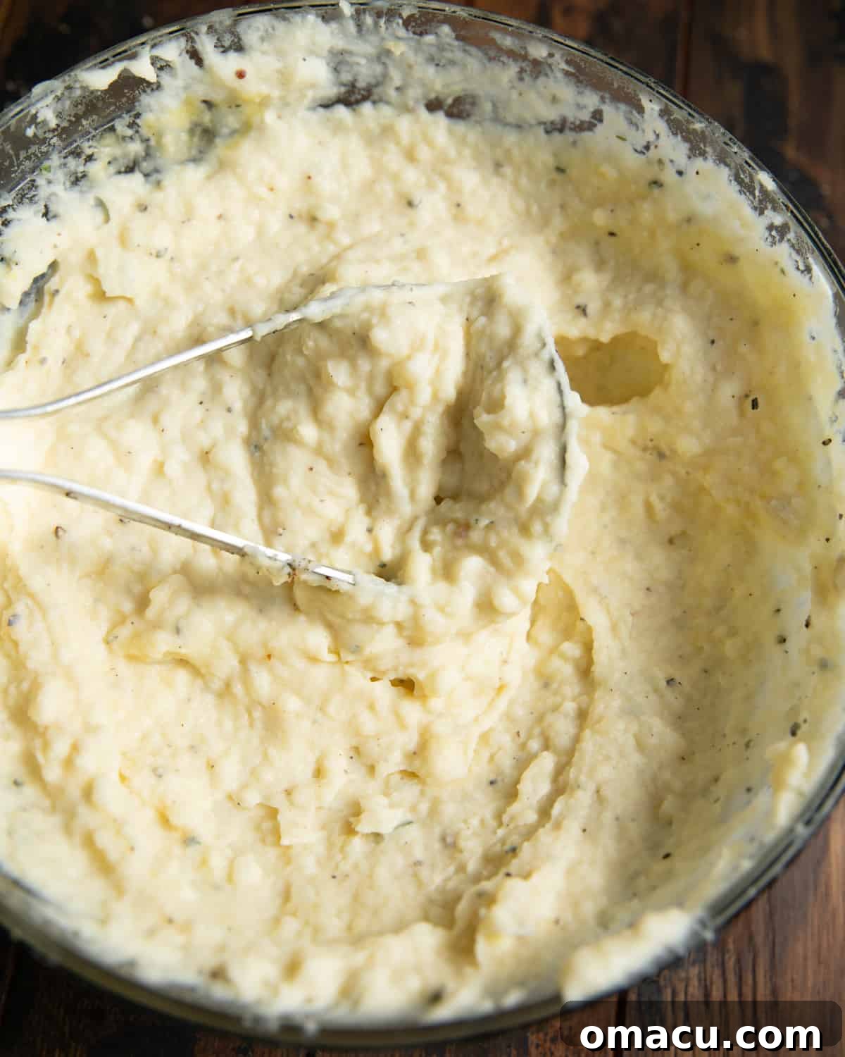 A potato masher in a mixing bowl of mashed potatoes.